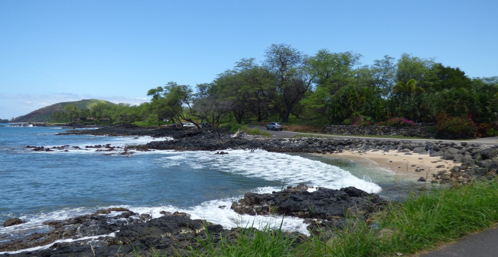 The South Maui coast along Makena Road: black lava coves, turquoise water, a small sand beach, kiawe trees, and a headland in the distance.